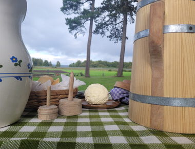 Ein Butterfass, daneben 1 Kugel Butter, 1 bemalter Krug auf einer grün karierten Tischdecke